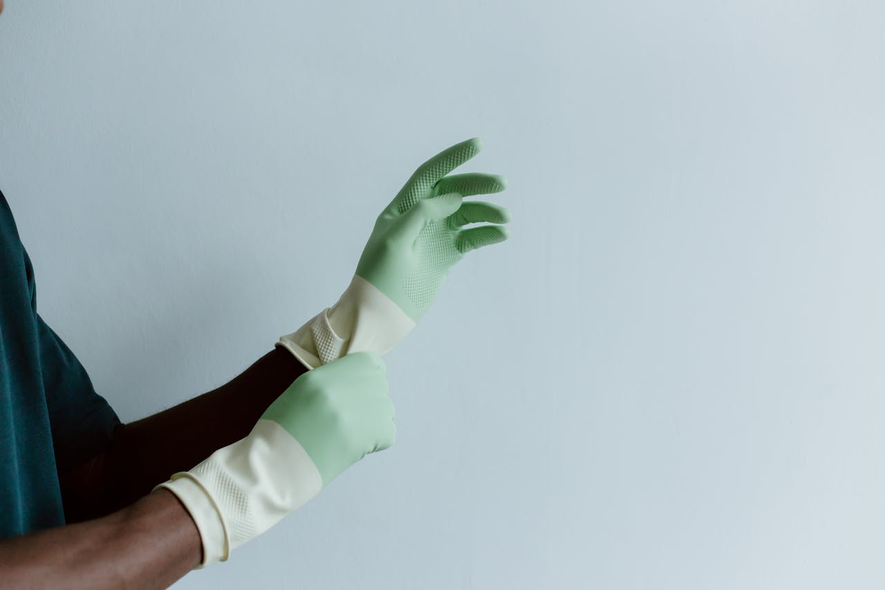 services-01 Close-up of a person putting on green latex cleaning gloves over a blue background.