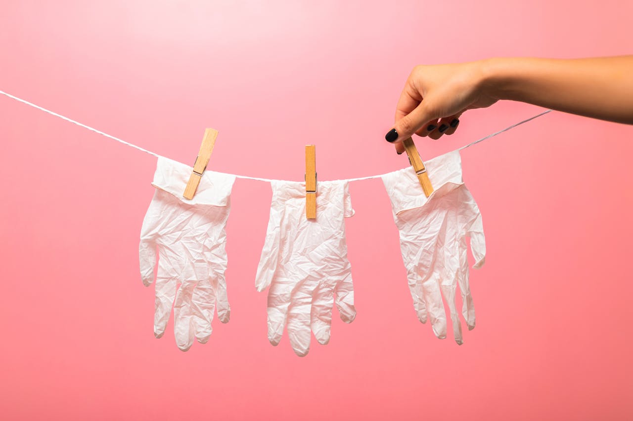 services-02 White medical gloves clipped to a line with clothespins against a pink backdrop, symbolizing hygiene.
