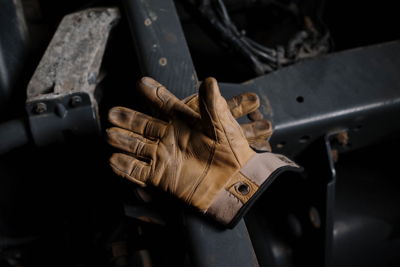 about-01 Close-up of worn leather gloves resting on machinery, suggesting hard work.
